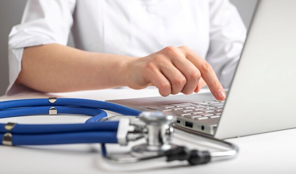 GP working at laptop, using computer at workplace. High quality photo
