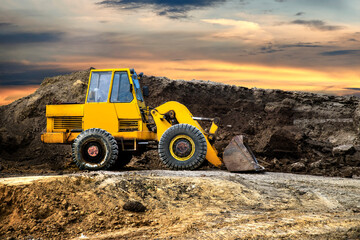 A bulldozer or loader moves the earth at the construction site against the sunset sky. Construction heavy equipment for earthworks