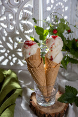 Ice cream with fresh strawberries and jam in waffle cone on plate, on rustic wooden background with a green napkin.