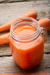 fresh carrot juice with carrots around old style wooden background