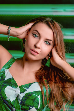 Portrait of stylish brown hair woman in green dress, green earrings, with makeup on green background in photostudio. Femininity, womanhood, travel, fashion concept