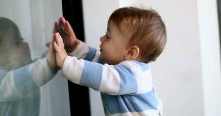 Toddler boy leaning on window reflection. Baby infant standing to window