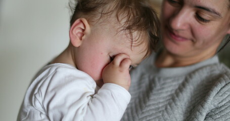 Tired mother and baby, mom yawning, infant wanting to sleep rubbing eye with hand