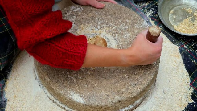 Woman is grinding wheat by hand in stone mill