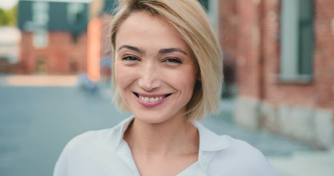 Close up portrait blond young attractive smile woman look at camera at city street. Outdoor portrait happy female girl.