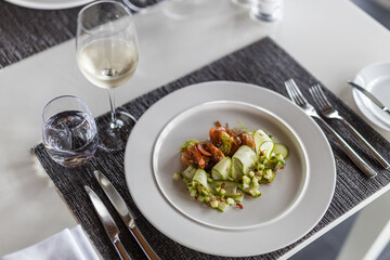 Luxury gourmet appetizer of cucumber rolls with shrimps and  closeup vegetables on elegant white plate. horizontal table top, white wine. Cuisine luxurious dinner salad, appetizer meal