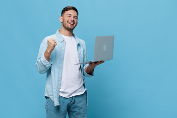 Overjoyed happy tanned handsome man in casual basic t-shirt rejoices at a successful win with laptop posing isolated on blue studio background. Copy space Banner Mockup. Electronics repair IT concept
