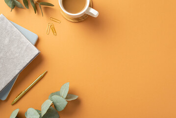 Business concept. Top view photo of workplace cup of coffee on wooden stand notepads stationery gold pen clips and eucalyptus leaves on isolated orange background with empty space
