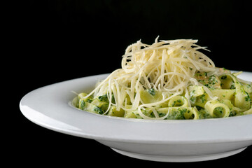 Spaghetti with cheese and herbs. On a white plate, black background.