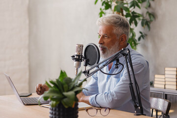 man records a podcast or interview with a microphone in a recording studio. an adult gray-haired...