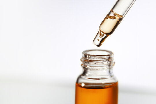Pipette with transparent fluid hyaluronic acid or serum. Cosmetics, science and healthcare concept closeup. Dose of serum or retinol falls in a bottle. Front view. Beauty product presentation, macro
