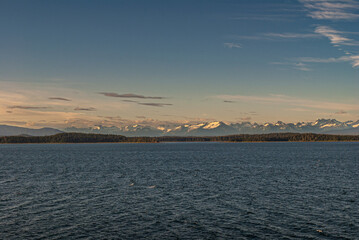 Skagway, Alaska, USA - July 20, 2011: Taiya Inlet above Chilkoot Inlet. Panorama combining blue cloudscape, sun lighted snowy mountain peaks, green forested belt separating all from blue ocean water