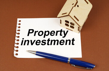 On a brown surface is a house, a pen and a notepad with the inscription - property investment