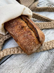 Macro photo of dark bread in ecological packaging against a wooden table.