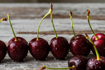Cherry berries in water drops close-up, lined up in a row on a light wooden surface
