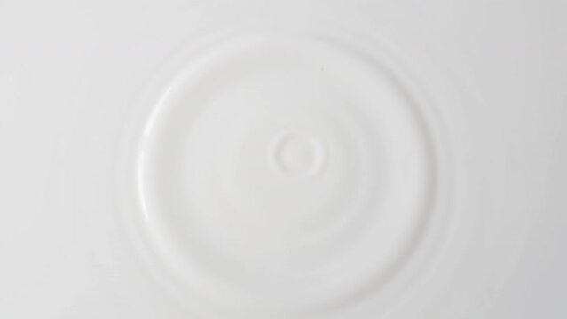 Drops of milk drip from top to center on a solid surface of milk close-up. Background of milk with falling drops. 4k raw slow motion video with speed ramp effect. Filmed on high speed cinema camera.