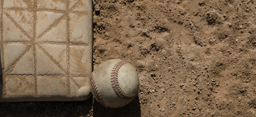 Baseball ball by base on dirt sports field close up, copy space on banner background.