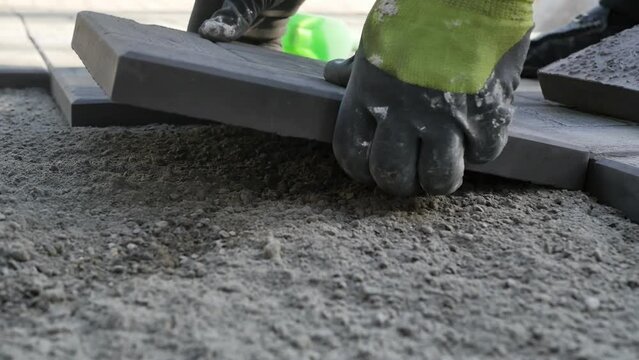 the builder's hands in work gloves lay the paving stones on even sand and knock on the tile with a heavy plastic hammer. Slow motion, detail