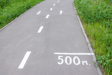 Fototapeta premium Bike path in a forest park with a marking of the center of the path, arrows for the direction of movement and distance from the beginning of the path.