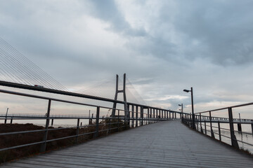 Fototapeta na wymiar Wooden pier with the Vasco da Gama Bridge on a gray overcast day in Lisbon