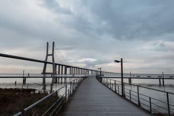 Beautiful view of the wooden pier, the long Vasque da Gama Bridge in cloudy weather. Journey to Lisbon, Portugal