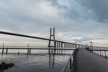 Fototapeta na wymiar Beautiful long bridge with a wooden pier and the sea against a cloudy sky. Vasco da Gama Bridge in Lisbon