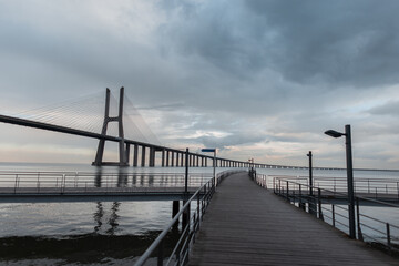 Fototapeta na wymiar Beautiful wooden pier and Vasque Dagama bridge with clouds in Lisbon, Portugal