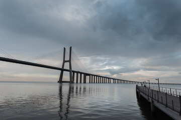 Amazing beautiful long Vasque Dagama Bridge with its pier and gray clouds in Lisbon, Portugal
