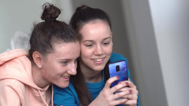 Two female friends having fun smiling looking at smartphone picture gallery