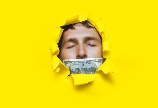 The man's face pokes out through a torn hole in the yellow paper, with a hundred dollar bill and a closed mouth. The concept of bribery, corruption, greed.Selling journalism, buying votes in elections