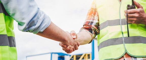 Close up handshake of two engineers on produce site. Group of industries workers meet on...