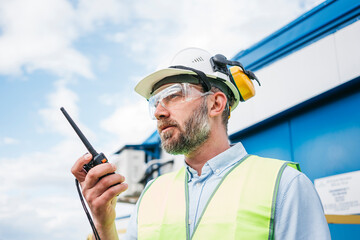 Man engineer wearing a helmet and protective glasses talk on walkie-talkie. Bearded engineer on produce site