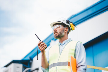 Portrait of engineer using walkie-talkie talking in production site. Bearded man worker control produce process