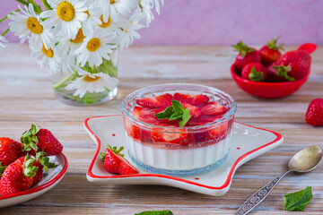 Dessert, creamy panna cotta with fresh strawberries in a glass flat bowl on a light wooden background. Dessert recipes without baking.