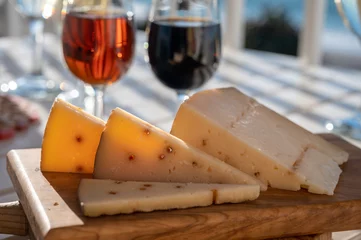 Fotobehang Spanish hard Andalusian cheese filled with Pedro Ximenez sweet sherry served outdoor with two glasses of sherry wine with blue sea on background © barmalini