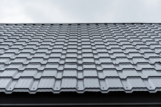 Metal tiles close-up, gray paint on the roof of the house, new construction of the upper floor, smooth lines of the corrugated board cell, the texture of the roofing material pattern.