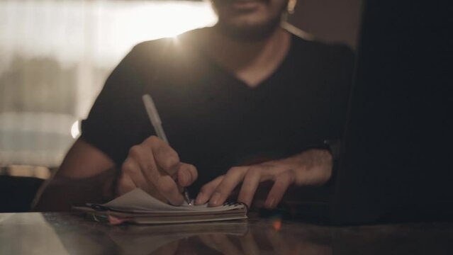 Man writing a book. Bright young man taking college classes at home. Business person jotting down innovative ideas and mapping out goals and objectives for his venture