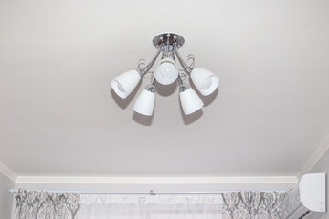 Chandelier with five arms on a white ceiling in a small room. Room lighting