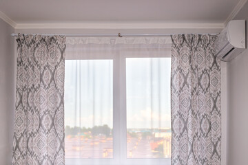 A window with a white tulle and a light curtain in an air-conditioned room overlooking the city....