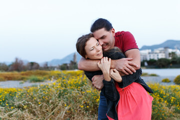 Shot of middle age woman being hugged by her boyfriend in grass field. Couple having fun on their summer holiday.