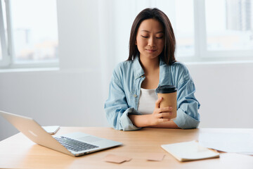 Happy smiling pensive young Asian cute businesswoman hold coffee cup enjoy looks aside in light office interior. Freelancer work at home. Lady corporation leader concept. Copy space Offer