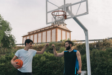 Happy young boys bumping fists after a street basketball game. Frontal image of a couple of sporty...