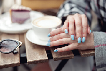 Obraz na płótnie Canvas Close up of female hands with blue manicure and cup of coffee at cafe. Cappuccino time.