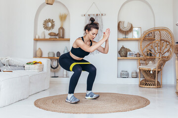 Woman working out at home doing squats with elastic band