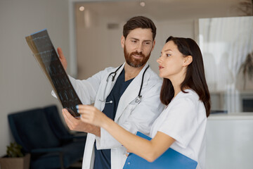 Two doctors in uniform look and discuss an scan of the patients spine