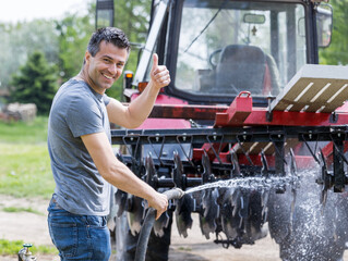 Farmer washing tractor with equipment on farm
