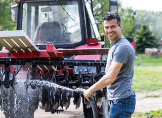 Farmer washing tractor with equipment on farm