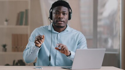 African man smiling blogger adviser teacher works in support service wears headphones talks at camera conducts educational webinar draws graphics line american millennial guy teaches students remotely - Powered by Adobe