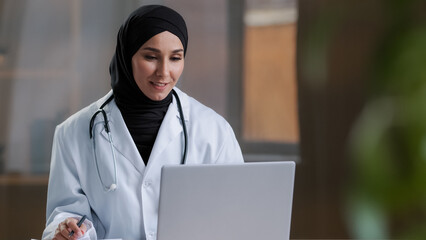 Arabian female therapist doctor wear hijab white coat calling distant patient on laptop talking with client in remote telehealth conference video chat giving online consultation virtual meeting visit