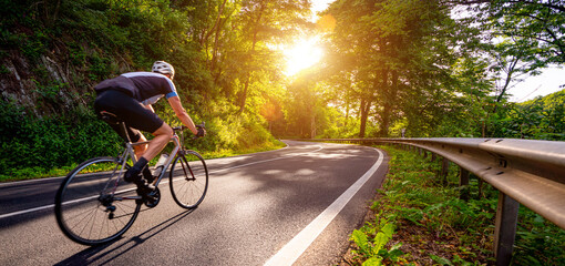 Mature Adult on a racing bike climbing the hill at forest landscape france country road - motion blur